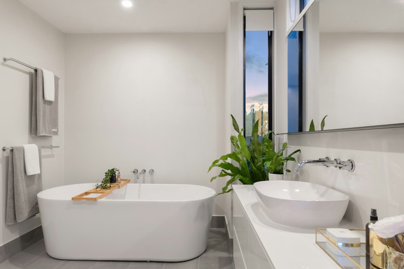 A bathroom with a freestanding bathtub, white vanity and green plants