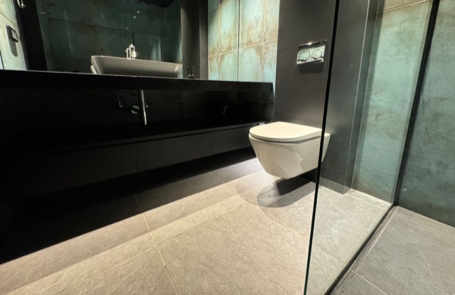 Dark-tiled bathroom with a floating vanity and frameless glass